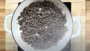 Cooked ground beef in a white pan on a wooden cutting board for a delicious meal preparation.